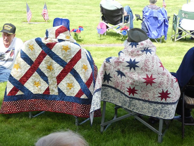 two seated veterans with their Quilts of Valor draped on the back of their chairs