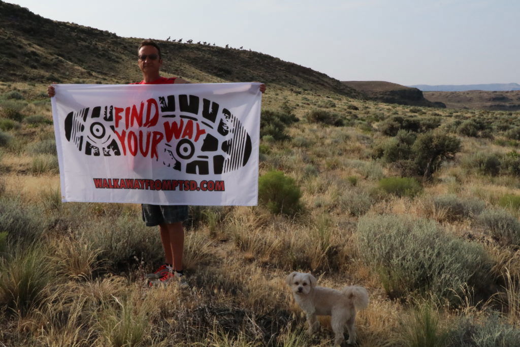 Rich Henning holding his Find Your Way banner in the sage-covered foothills of central Washington