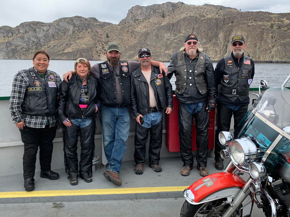 group of motorcycle riders posing on a bridge overlooking a river with mountains in the background